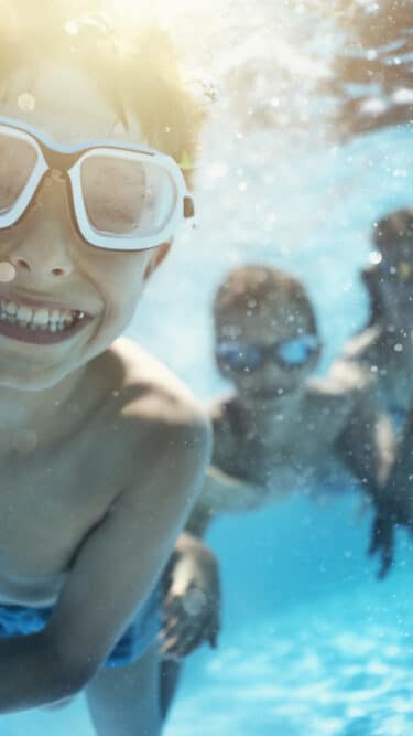 Happy kids having underwater party in the swimming pool. The boy is grinning at the camera. 
Shot with Nikon D850.